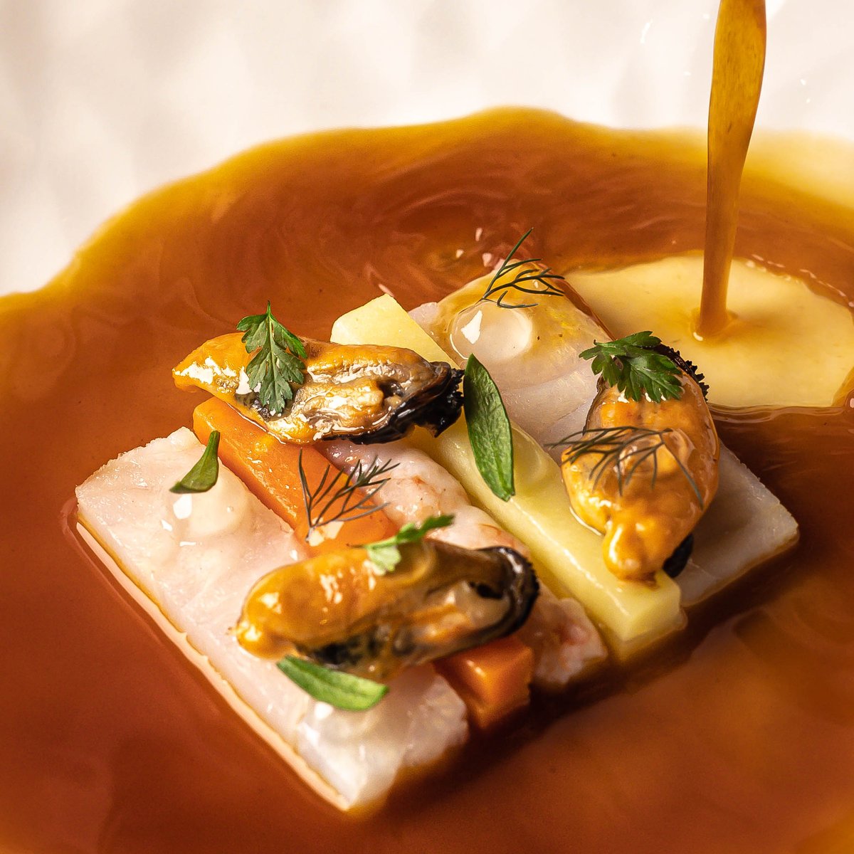 Un poisson servi dans son bouillon ambré, coquillages et herbes, la cuisine de Contraste